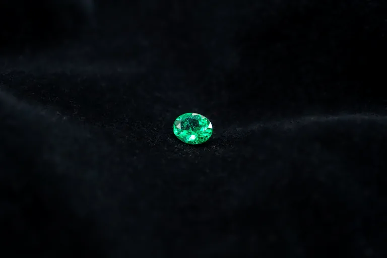 A loose oval Colombian Muzo emerald on black silk