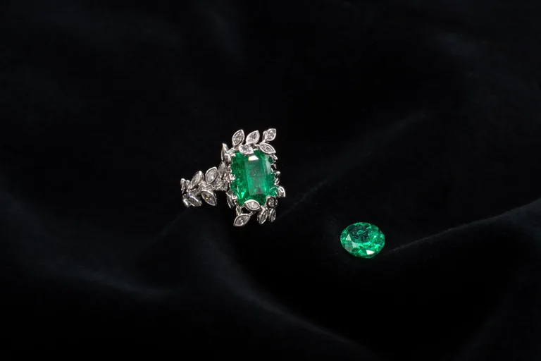 An emerald-cut Muzo emerald set in a diamond halo ring beside a loose emerald