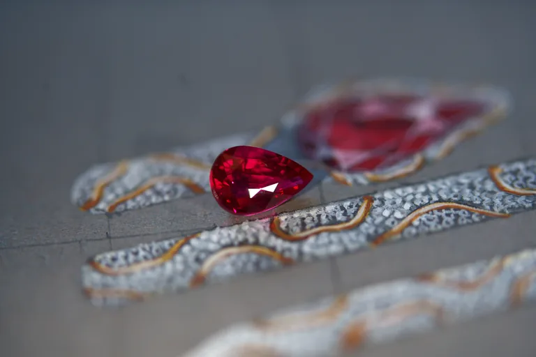 A pear-shaped ruby resting on a gouache painting of a serpent ring
